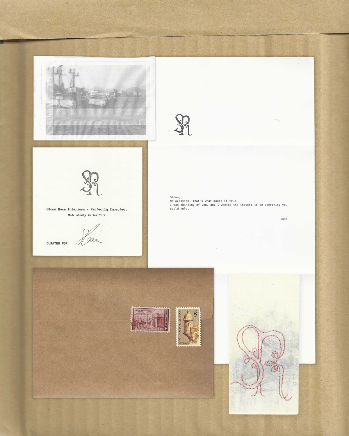 Flat lay of Sloan Rose Interiors gifting stationery on kraft cardboard: a vintage harbor photocopy, a cream notecard with the SR monogram reading "Perfectly Imperfect, Made slowly in New York," a typewritten "no occasion" love letter signed Rose, a stamped kraft envelope, and a tag with the SR monogram hand embroidered in red thread.